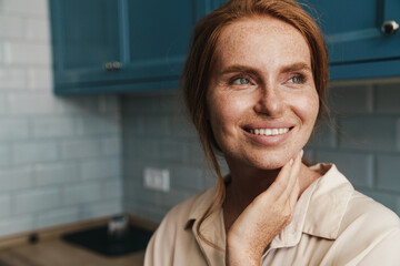 Image of happy redhead woman smiling and looking aside while standing