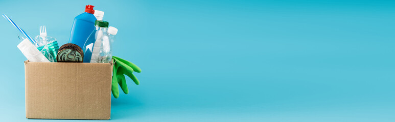 plastic rubbish and rubber gloves in cardboard box on blue background, panoramic shot