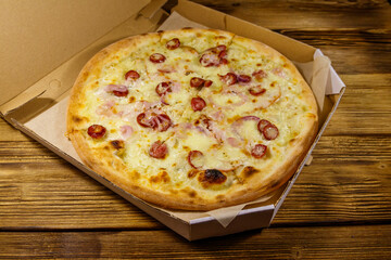 Delicious fresh pizza in cardboard box on a wooden table. Concept for home delivery of food, fast food, delivery of pizza