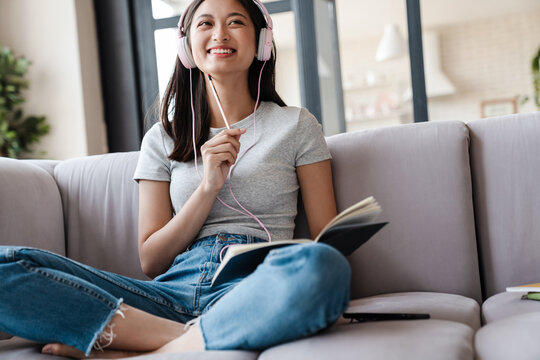 Image of smiling asian woman using headphones and writing down notes