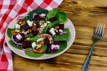 Tasty spinach salad with boiled beetroot, feta cheese, walnut and red onion on wooden table. Healthy vegetarian food