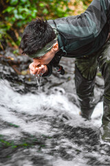 Soldier or revolutionary member or hunter in camouflage near the stream drinking natural clean water from the stream