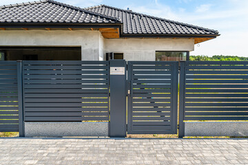 Modern panel fencing in anthacite color, visible wicket with videophone and a house in the background.