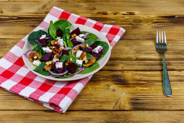 Tasty spinach salad with boiled beetroot, feta cheese, walnut and red onion on wooden table. Healthy vegetarian food