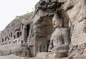 Iconic seated Buddha statue in Cave 20 & caves in weast part at Yungang Grottoes, Datong, Shanxi, China. Constructed from 5th century in Northern Wei period. UNESCO World Heritage.