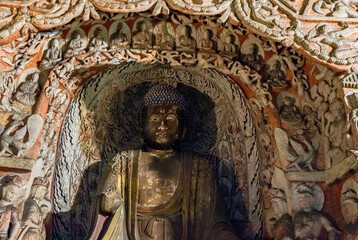 Colored Buddha statue in a niche of Cave 6 with frescos & Buddhist sculpture at Yungang Grottoes, Datong, Shanxi, China. Created from 5th century during Northern Wei period. UNESCO World Heritage.