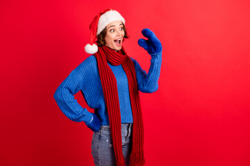 Photo of positive cheerful crazy childish girl in santa claus cap have communication with her mittens talk speak wear sweater isolated over red bright shine color background