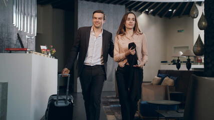 Businessman taking room key at hotel reception. Traveling couple settling hotel