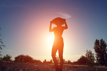 Silhouette of a beautiful woman in an Asian conical hat on the background of the sunset.