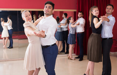 Young smiling people learning to dance waltz in dancing class