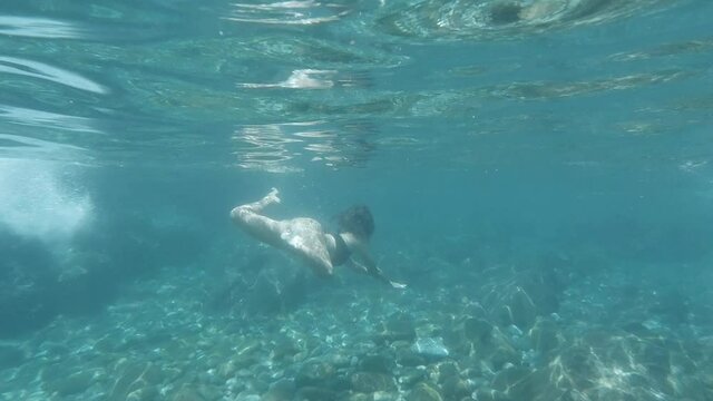 slow motion underwater back view of young adult woman swimming in ocean
