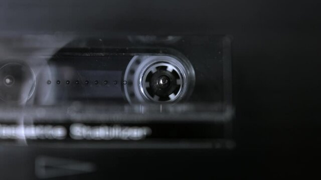 An audio cassette spools tape in extreme macro. Shallow depth of field with focus on the rorating spool. Suggests an interrogation or phonetap. 