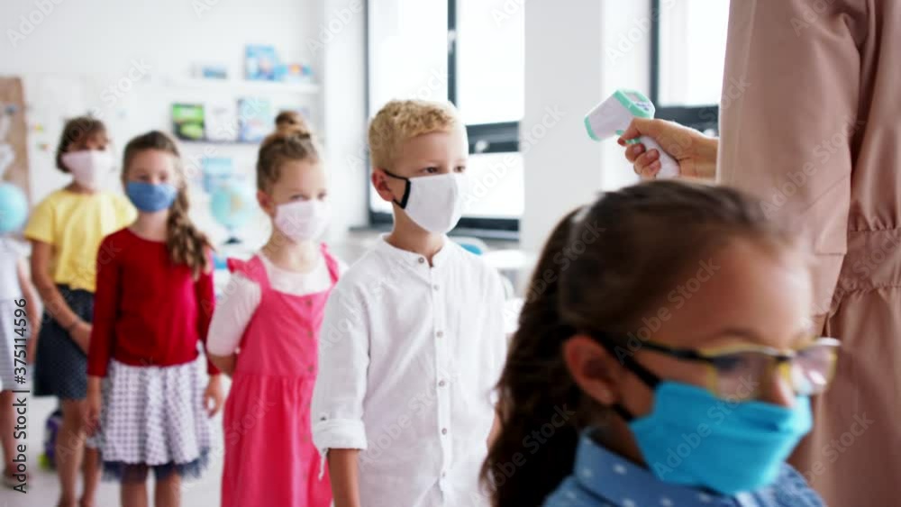 Wall mural Teacher and children with face masks indoors in classroom, measuring temperature.