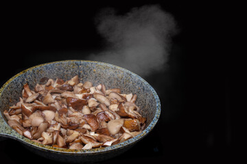 Close-up of fried or stewed mushrooms in a skillet, steam rises from hot mushrooms, isolated on black background