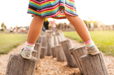 Child does balance exercise on wooden pegs. Little girl balances on logs.
Kleines Mädchen balanciert auf Holzstämmen. Kind macht Gleichgewichtsübung auf Holzpflöcken.