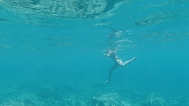 slow motion underwater side view of blond young adult woman swimming in ocean