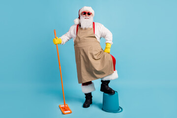 Cleaning hero. Photo of pensioner old man grey beard hold mop leg bucket self-assured wear santa x-mas costume apron rubber glove suspender sunglass cap isolated blue color background