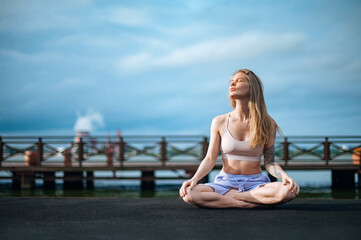 Fototapeta na wymiar Yoga practice and meditation in nature in sunrise. Woman practicing near City on pier.