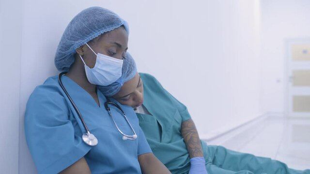 Depressed female medical workers sitting on floor sleepy after shift, friendship