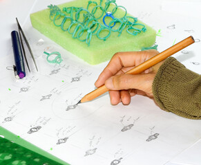Jewelry designers are drawing sketches on paper and wax molds placed on the table.