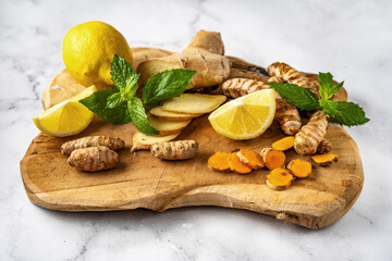 Close up of wooden board with ginger, turmeric, lemons and mint