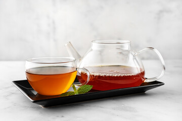 A glass cup of ginger tea with kettle on black plate and white background