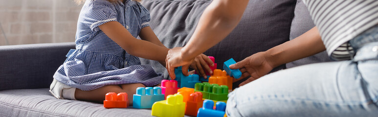 cropped view of african american babysitter and child playing with colorful building blocks on sofa, horizontal image - obrazy, fototapety, plakaty