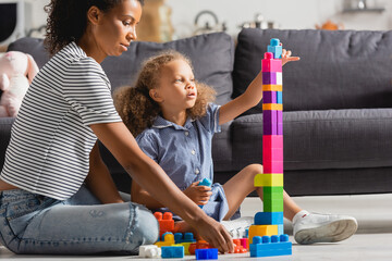 african american child sitting on floor near babysitter and building tower from multicolored blocks