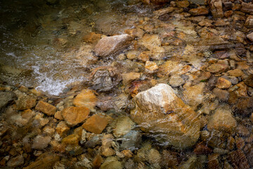Brown rocky creek surrounded by crystal clear water at a small water fall