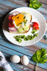 Vertical view of fried eggs with bacon and vegetables on bun bread with condiments