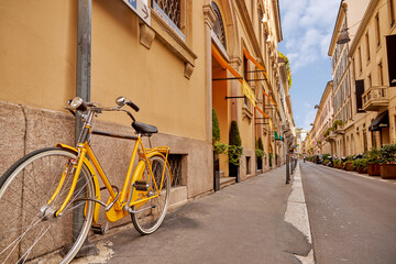 A beautiful bright yellow bicycle stands on a beautiful old street. Cycling around the cities of Europe. Historic old buildings. Narrow street. Milan Italy 08.2020