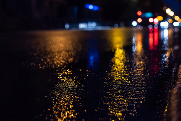 selective focus of city road and car during rain at night, with unfocused lights from headlights of cars. Water from rain and abstract image of side lights in city