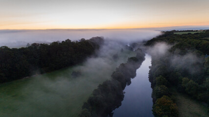 Aerial view of misty morning river during sunrise, rural Ireland landscape.