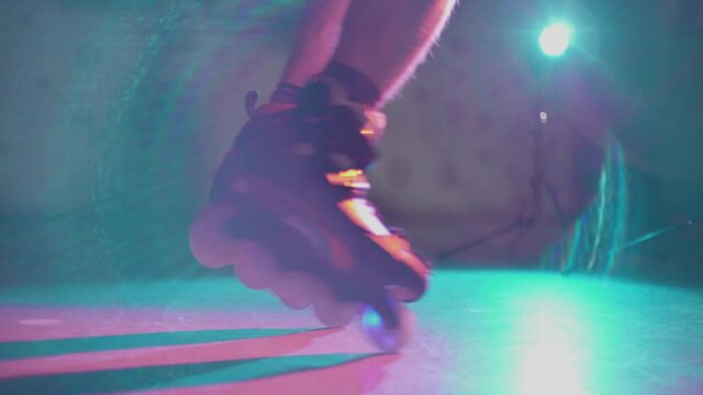 Guy spinning on roller skates on spotlight in dark place. Teenager showing skills on freeskate. Young male example of active nightlife youth culture. Concept of extreme, lifestyle, sport.