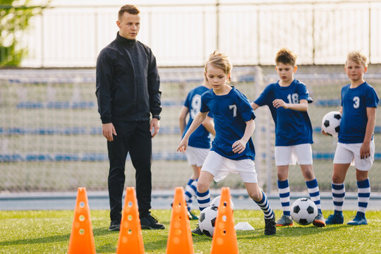 Kids in soccer team on practice session with young coach. Boys young athletes training football on grass field. Kids kicking balls and running fast during soccer training camp