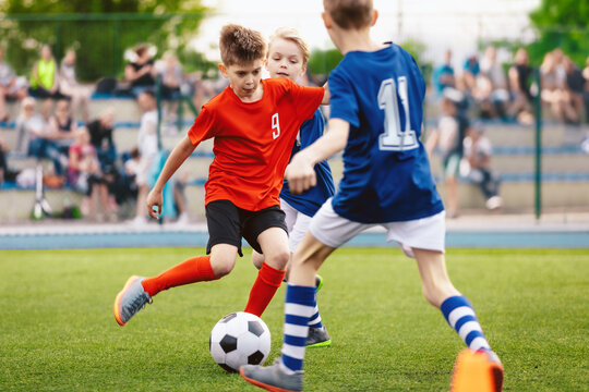 Boys play soccer game. Junior competition between players running and kicking soccer. ball. Youth junior athletes in red and blue soccer shirts. Kids compete in elementary school sports tournament