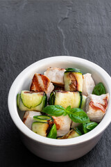 Grilled chicken and zucchini roll in clay bowl on black stone background