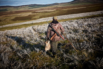 A hunter with his trophy after a big hunt in Scotland. Walking in the highlands with a dead deer's...