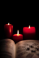 Old book with tarot cards and red candles in front of black background, reading horoscope and fortune