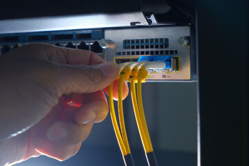 Hand of system engineer and fiber optic cable connected to enclosure box in a technology data...