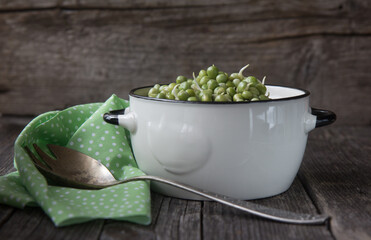 Sprouted green peas in a white bowl on a green napkin and wooden background.