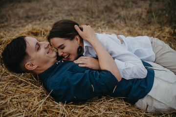 Couple in love lays in haystack on meadow and has fun.