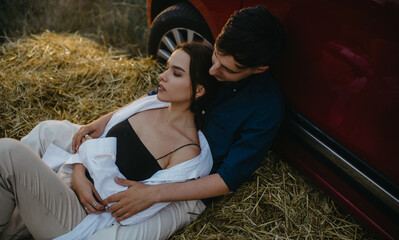 Couple in love rests on haystack near car.