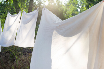 white bedding, clothesline drying, hanging outside. Against the background of the rays of the setting sun - Powered by Adobe