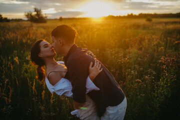 Couple in love embraces and kisses on meadow at sunset.