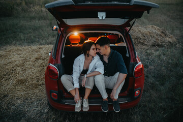Couple in love sits and rests inside of opened trunk of car.