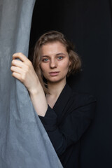 portrait of young caucasian woman with short hair posing in black suit jacket, holding curtain. closeup shot of pretty girl. short-haired attractive female poses in studio