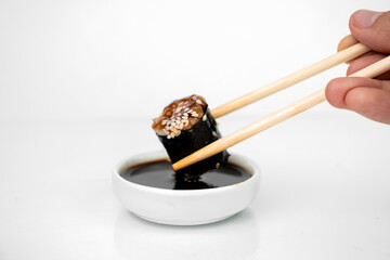 take an unagi maki rolls with bamboo chopsticks and put it into soy sauce on white background, asian food, japanese cuisine