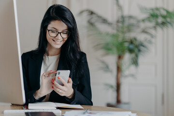 Beautiful smiling female freelancer works remotely, concentrated in smartphone, sends feedback on...