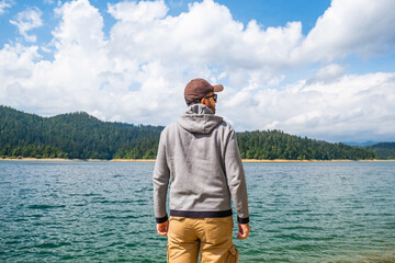 Man in cargo pants and hoodie standing on lake shore and observing the surface, Lokvarsko lake,...